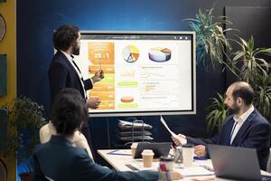 General director showing statistics data on interactive board in a conference, briefing meeting with workers for a presentation. Workmates studying sales reports to adapt within market conditions. photo