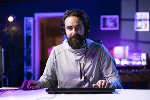 Smiling professional gamer in studio teaching viewers strategies to beat opponents during livestream. Happy content creator streaming live from RGB lit home, filming videogames guide photo
