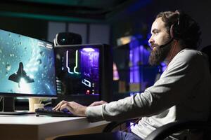 Man using gaming keyboard and headphones to play spaceship flying game with overlay HUD showing health, fuel bars. Gamer wearing headset navigating with spacecraft in galaxy, shooting at asteroids photo