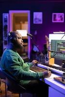 Professional artist writes new verses for a song in home studio, producing new music with mixing console and pc software. Composer works with audio equipment and tools, recording tunes. photo