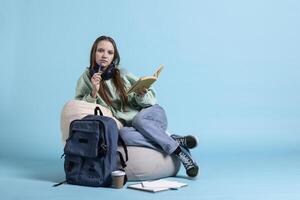 Portrait of girl perplexed by confusing information on textbook, preparing for high school exams, studio background. Woman puzzled by difficult homework, doing thinking gesturing on beanbag photo