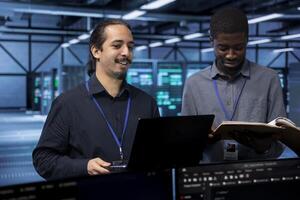 Cheerful IT specialists in server hub ensuring data remains shielded from potential threats. Smiling coworkers safeguarding data center against unauthorized access using laptop photo