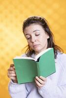 Woman feeling unimpressed while reading bad book, enjoying hobby during leisure time. Bookaholic person with dull novel in hands disappointed by boring story, isolated over studio background photo