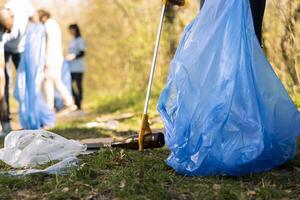 Volunteers group gathering to tidy up the woods of garbage, fighting forest pollution to protect the natural ecosystem. Team of activists collecting rubbish and plastic waste with tools. photo