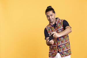Indian man playing videogames on cellphone in landscape mode, enjoying leisure time. Smiling gamer enjoying game on mobile phone, having fun, isolated over studio background photo