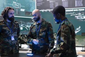 Diverse team of recruits examining information on a hologram, working with federal CCTV satellite system in monitoring room army base. Intelligence gathering activity on holographic projection. photo