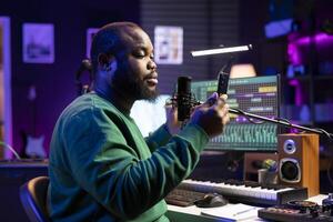 African american producer singer recording audio of his track, adding effects and editing with a stereo console to improve sound quality. Young composer artist performing song on microphone. photo