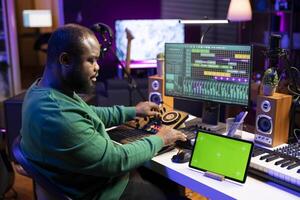 Confident musician producing tracks on mixing console in home studio, using isolated mockup screen and editing music in post production. Artist performer creating new beats for his songs. photo