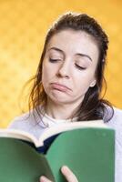 Woman pouting while reading soppy book, enjoying hobby during leisure time. Bookaholic person with novel in hands glooming, upset by character death, isolated over studio background photo
