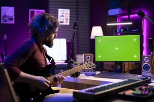 Artist playing acoustic guitar and following tutorials online on computer that shows greenscreen display. Music producer learning new instrument and accords to record tunes on daw software. photo