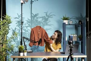 Content creator presents fast fashion jacket to viewers, filming haul with smartphone on tripod and mic. Fashion vlogger engaging subscribers with shopping haul, doing affiliated marketing photo