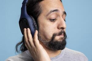 Relaxed person enjoying music on headphones expressing joy for leisure activity. Modern adult showcases enjoyment of audio entertainment and wireless gadgets in a professional studio. photo