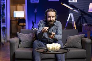Man having fun playing videogames on gaming console while talking with teammates using headphones mic. Gamer battling rival players using controller, chatting with friends through headset microphone photo