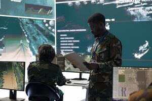 Military control tower personnel monitoring air traffic activity in command post, examining data from case files and big screen. Soldier collects information from reconnaissance system. photo