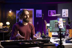 Producer doing online paid classes to help people play piano, teaching lessons from his home studio and recording tutorial. Skilled instructor playing midi controller synthesizer, explaining notes. photo