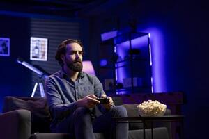 Gamer engaging in online competitive multiplayer tourney using cutting edge gaming console and gamepad. Man in home theatre playing engaging videogame, focused on defeating enemies photo