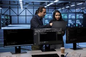 Coworkers in server hub establishment confused by errors on laptop screen. Perplexed admins shocked by system bugs while safeguarding data center equipment against malware photo