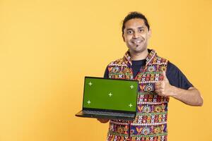 Portrait of jolly tech expert presenting green screen laptop, doing thumbs up gesturing, studio background. Upbeat person doing positive hand gesture while reviewing chroma key notebook photo