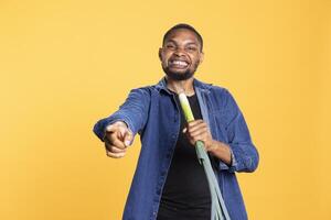 African american funny man singing with a leek pretending it is a microphone, advertising healthy eating and having fun. Confident carefree model fooling around in studio with food. photo