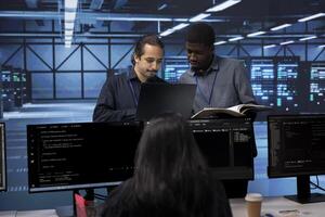 Diverse team of engineers in data center looking for firewall misconfigurations affecting servers. Multiracial workers in server room check systems bottlenecks leading to sluggish data transfer rates photo