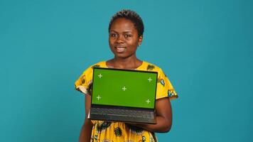Natural smiling woman posing with a green screen on laptop, making an advertisement with isolated mockup display in studio. Young traditional person in tribal native clothing. Camera A. photo