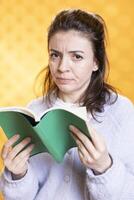 Woman frowning while reading book, upset by story, spending time on hobby. Bookaholic person with novel in hands critical of plot and characters, enthralled by emotional story, isolated over studio background photo
