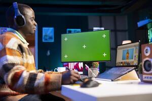 Black expert photo editor working remotely in a creative industry, using his skills and software tools on dual monitors to edit images with precision. Working on a freelance retouching project.