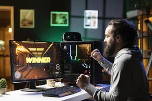 Happy man celebrating after completing videogame in neon lit living room. Smiling gamer having gaming session, ecstatic about victory while competing in multiplayer tournaments photo