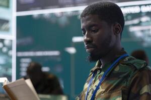 Army soldier reading a new defense operation case file in military headquarters, using reconnaissance CCTV footage on a big screen. Recruit tracking location of deployed troops. Close up. photo