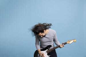 Enthusiastic rocker playing a black electric guitar with passion and joy for rock and roll music. Dynamic, trendy performer with long hair brings movement, fun and entertainment to the studio. photo