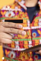 Man uses tablet and debit card to do online purchases during promotional sales period. Close up shot of person wearing traditional indian attire does internet shopping using digital device photo