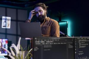 Programmer scratching head in confusion trying to secure company servers from virus attacks. Hesitant IT remote employee unsure how to fix code, trying to building firewalls protecting data photo