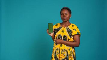 Young confident woman presenting a green screen on smartphone, working in studio on an advertisement. Smiling natural girl holds a phone with isolated chroma key display. Camera B. photo