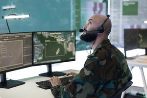Army soldier operating on a surveillance CCTV system connected to a big screen in federal monitoring room, examining air and sea traffic on reconnaissance servers. IT operator in base. Close up. photo