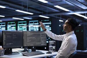 Software developer looking at holograms in data center, monitoring infrastructure. Man in server room interacting with high tech augmented reality AI visualization to do maintenance on hardware photo