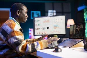 African American man having discussion during online meeting on laptop, talking about internet statistics or data. Male freelancer use technology for virtual communication, working remotely. photo