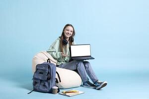 Smiling woman scrolling on isolated screen laptop to check social media feed, relaxing on beanbag. Happy teenager browsing internet websites on mockup device, studio background photo