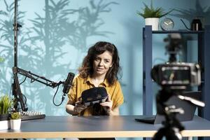 Futuristic VR goggles held by tech specialist reviewing them for viewers. Internet star filming technology channel vlog for gadget enthusiasts, showcasing virtual reality headset photo
