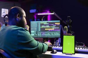 Sound engineer composing new tunes with daw interface, operating on greenscreen display. African american skilled musician mixing and mastering his recordings, stereo console and gear. photo