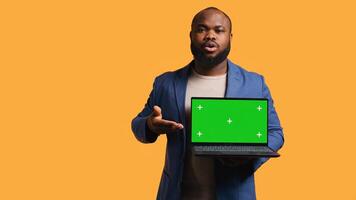 Portrait of african american man doing influencer marketing using green screen lapyop, studio background. BIPOC person holding empty copy space mockup notebook, doing advertising camera B photo