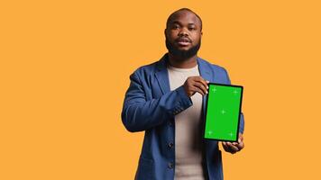 Portrait of african american man doing influencer marketing using green screen tablet, studio background. Smiling BIPOC person holding empty copy space mockup device, camera B photo