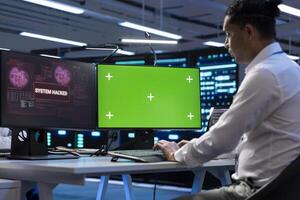 Technician in server farm using isolated screen PC to stop hacker passing company firewall and stealing sensitive user data. IT staff member looking at chroma key computer, seeing security breach photo