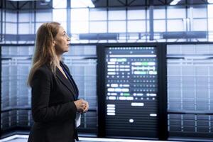 Engineer walking between server rows in data center, doing yearly infrastructure inspection. System administrator in high tech server hub monitoring supercomputers equipment photo