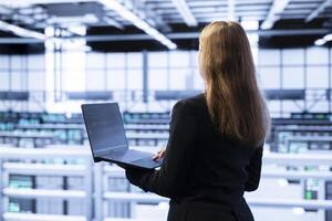 Technician using laptop in data center to do disaster recovery planning and security protocol enforcement. Woman in server room to working to reduce equipment downtime, ensuring business continuity photo