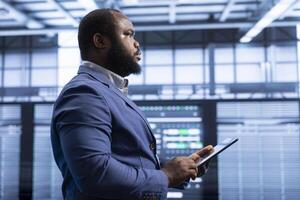 Supervising manager in data center implements backup solutions to protect against data loss using tablet, ensuring efficiency. High tech establishment IT expert resolving technical issues using device photo