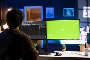 Programmer doing software debugging on green screen PC at home, checking broken lines of code displayed on monitors. IT professional in living room fixing coding problems on mockup computer photo