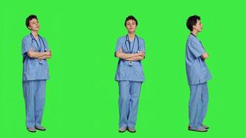 Portrait of smiling medical assistant poses with arms crossed, showing confidence dressed in blue hospital scrubs. Successful nurse standing against greenscreen backdrop, health specialist. Camera A. photo