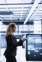 Software developer using tablet in data center with advanced tech, ensuring cybersecurity and efficient network management. Woman in server hub optimizing data center hardware with device photo