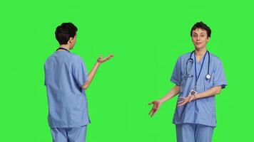 Healthcare specialist presenting a thing for promotional ad in studio, pointing at something against greenscreen backdrop. Medical assistant creating a web commercial, health expertise. Camera B. photo