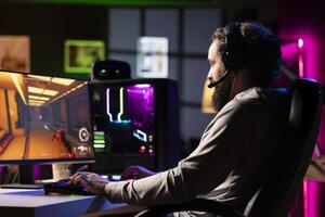 Man relaxing by playing futuristic science fiction videogame on PC at computer desk, using headphones. Gamer shooting enemies with lasers in online multiplayer shooter, hearing immersive sounds photo